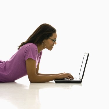 Side view of African American mid adult woman lying on floor using laptop.