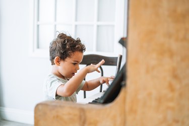 Little curly haired boy playing piano in living room at home