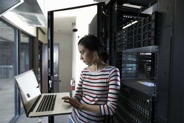 Female Filipino IT technician working at laptop in server room