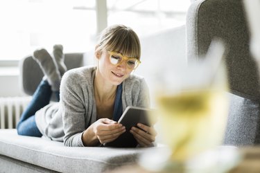 Smiling woman lying on couch using tablet