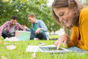 Student using tablet PC while males using laptop in park