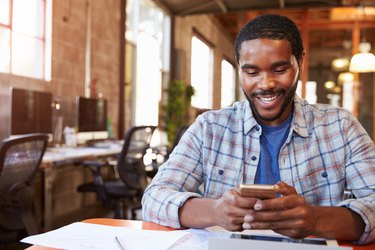 Designer Sitting At Meeting Table Texting On Mobile Phone