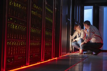 IT technicians talking at glowing panel in dark server room