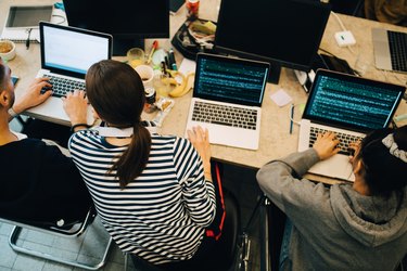 High angle view of young computer programmers coding on laptops at desk in small office