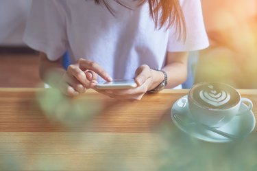 Young girl holding a white phone has a blank screen in cafe, And coffee on the table to make life more relaxing. The use of technology for a happy life.