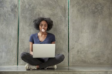 African American college student using laptop and blowing bubble gum bubble