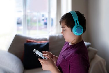 Primary school Kid using mobile phone searching information on internet for homework,Child wearing headphone studying online with teacher,Home schooling,E-learning education,Children with technology