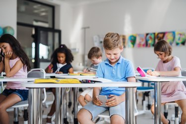 A small school boy with smartphone sitting at the desk in classroom, playing.