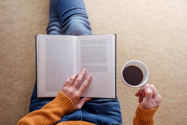 Midsection Of Woman Having Drink While Reading Book On Carpet